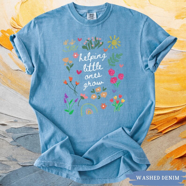 May include: A light blue t-shirt with a white graphic design of flowers and the text "helping little ones grow".