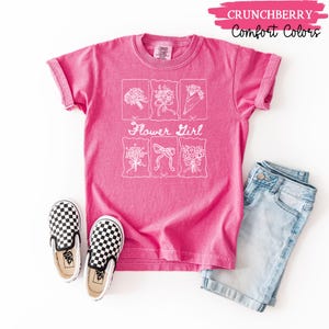 May include: A bright pink t-shirt with the words "Flower Girl" and six floral illustrations in white. The shirt is paired with light blue denim shorts and black and white checkered slip-on shoes. The text "Crunchberry Comfort Colors" is at the top.