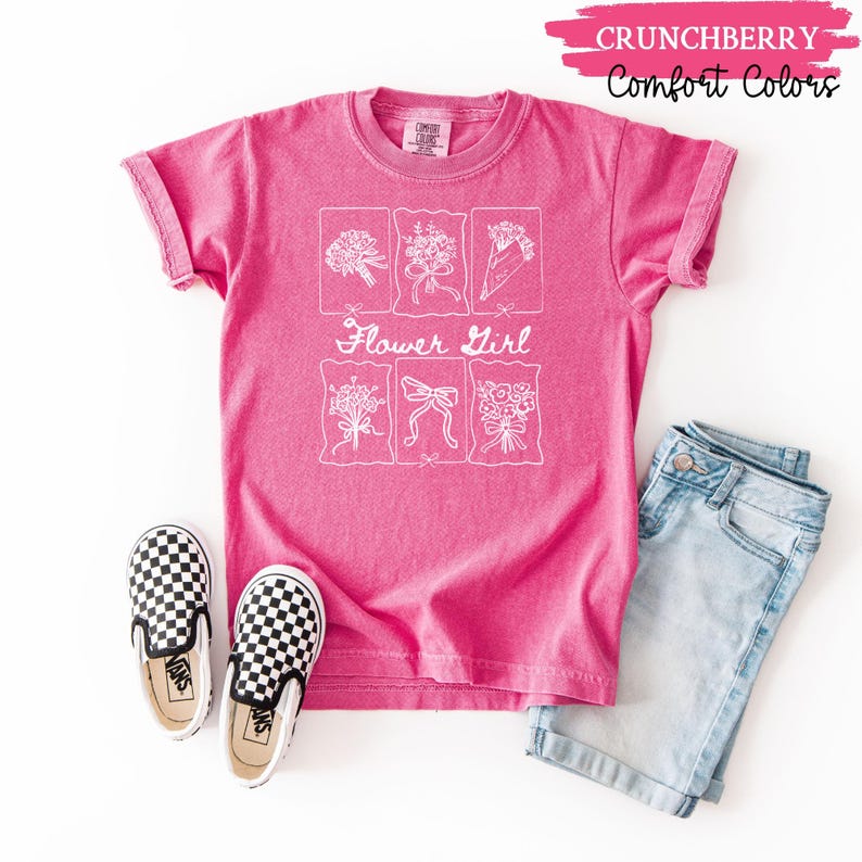 May include: A bright pink t-shirt with the words "Flower Girl" and six floral illustrations in white. The shirt is paired with light blue denim shorts and black and white checkered slip-on shoes. The text "Crunchberry Comfort Colors" is at the top.