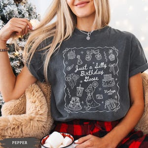 May include: Dark gray t-shirt with a white graphic that says "Just a Silly Birthday Goose" with birthday-themed illustrations. The shirt has short sleeves and a relaxed fit. The word "Vintage" and the year "1995" are also included in the graphic.