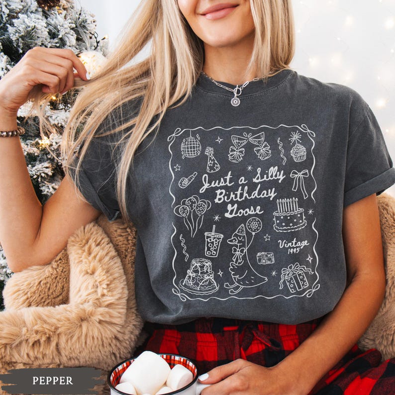 May include: Dark gray t-shirt with a white graphic that says "Just a Silly Birthday Goose" with birthday-themed illustrations. The shirt has short sleeves and a relaxed fit. The word "Vintage" and the year "1995" are also included in the graphic.