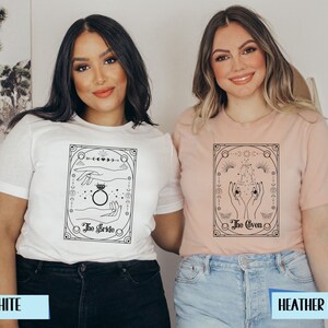 May include: Two t-shirts with a black and white graphic design. The graphic features a hand with a ring and the text "The Bride" on one shirt and a hand with the text "The Coven" on the other. The shirts are available in white and heather peach.