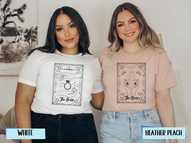 May include: Two t-shirts with a black and white graphic design. The graphic features a hand with a ring and the text "The Bride" on one shirt and a hand with the text "The Coven" on the other. The shirts are available in white and heather peach.