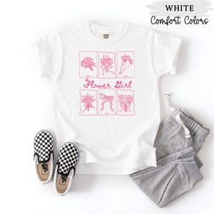 May include: White t-shirt with a pink floral design and the words "Flower Girl". The shirt is paired with gray sweatpants and black and white checkered slip-on shoes. The words "WHITE" and "Comfort Colors" are printed at the top.