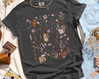 May include: A dark gray t-shirt with a floral print featuring squirrels and leaves. The print is in shades of pink, brown, and green.