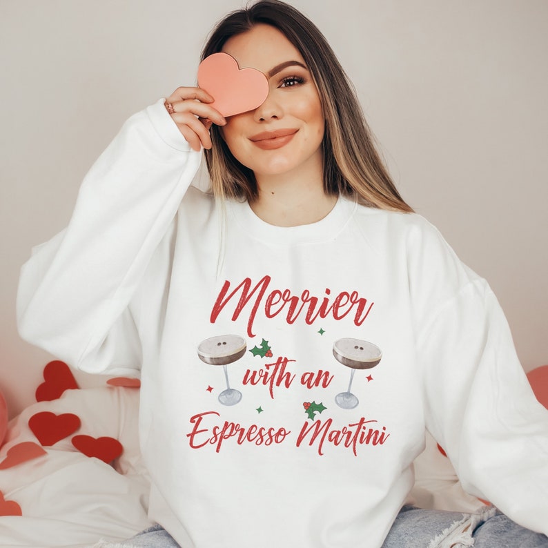 May include: White sweatshirt with red text that reads "Merrier with an Espresso Martini" and two illustrations of espresso martinis with holly sprigs.