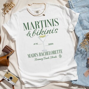 May include: White t-shirt with green text that reads "Martinis & bikinis" with a martini glass illustration and the text "June 2026 Madi's Bachelorette Rosemary Beach, Florida".