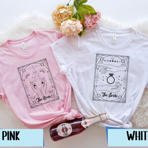 May include: Two t-shirts with a black and white graphic design. The pink t-shirt has the text "The Coven" and the white t-shirt has the text "The Bride".