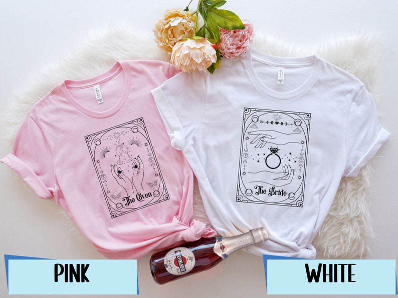 May include: Two t-shirts with a black and white graphic design. The pink t-shirt has the text "The Coven" and the white t-shirt has the text "The Bride".