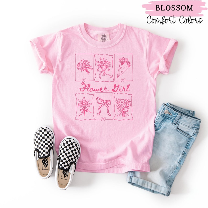 May include: A light pink t-shirt with a floral design and the words "Flower Girl". The shirt is paired with denim shorts and black and white checkered slip-on shoes. The text "Blossom" and "Comfort Colors" are also visible.