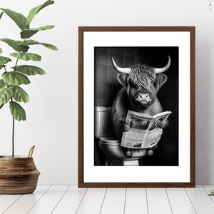 May include: A black and white photograph of a Highland cow sitting on a toilet and reading a newspaper. The cow is wearing a serious expression and has a long, shaggy coat.