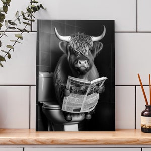 May include: Black and white canvas print of a Highland cow sitting on a toilet, reading a newspaper. The newspaper is open, displaying the text "The New York Times". The cow has long, shaggy fur and large horns.