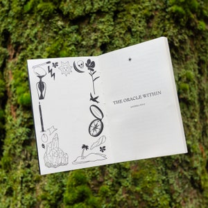 May include: A white book with a black and white illustration of a compass on the front cover. The title of the book is "The Oracle Within" by Andrea Wan.