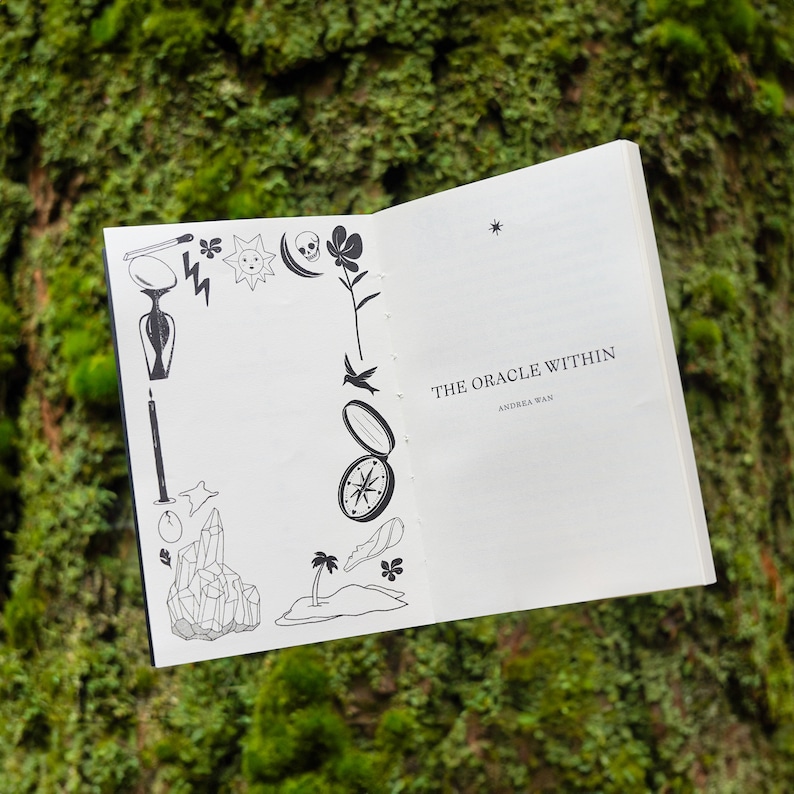 May include: A white book with a black and white illustration of a compass on the front cover. The title of the book is "The Oracle Within" by Andrea Wan.