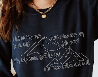 May include: A navy blue sweatshirt with a white graphic of mountains and the text "I lift up my eyes to the hills. From where does my help come? My help comes from the Lord, who made heaven and earth."