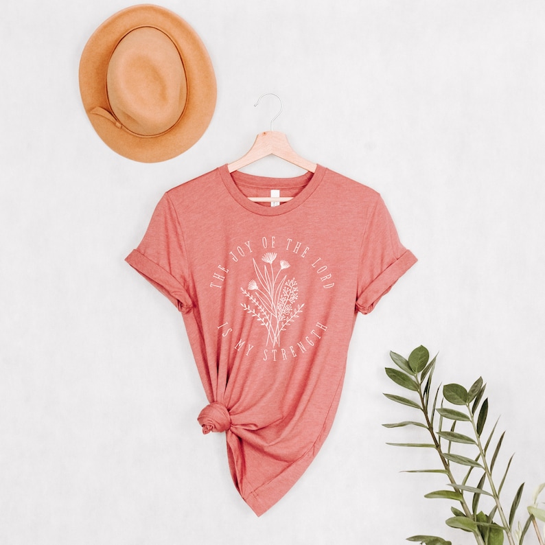 May include: A coral pink t-shirt with the text "The joy of the Lord is my strength" in white lettering with a floral design.