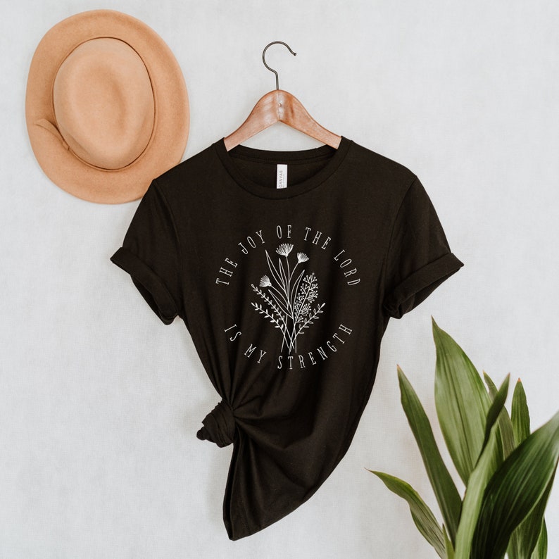 May include: Black t-shirt with a white floral design and the text "The joy of the Lord is my strength".