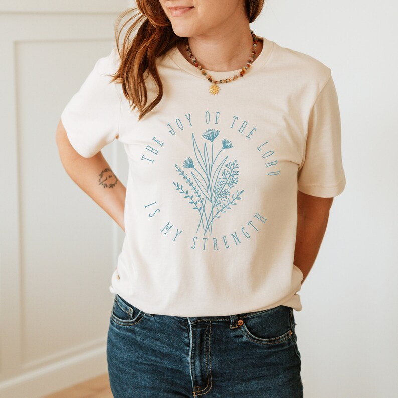 May include: A white t-shirt with a blue floral design and the text "The Joy of the Lord is My Strength".