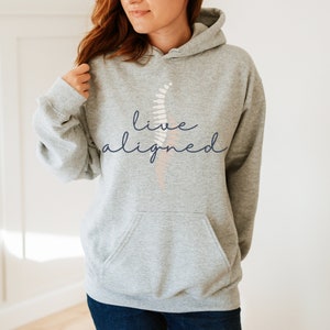 May include: Gray hooded sweatshirt with the text "live aligned" in navy blue script. A stylized pink and white fern design is behind the text.