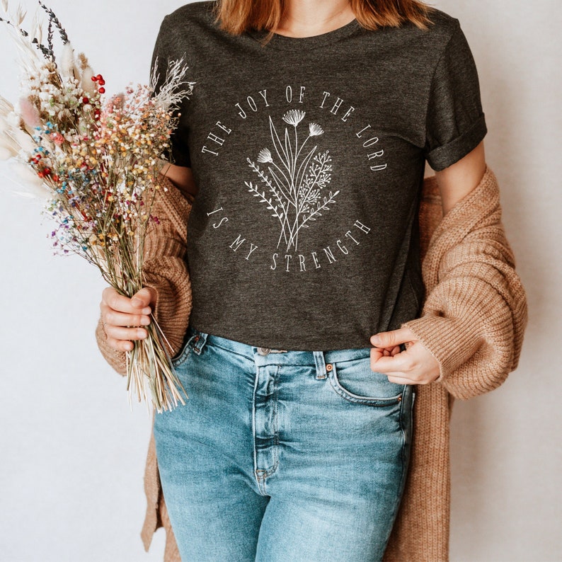 May include: A dark gray t-shirt with a white floral design and the text "The Joy of the Lord is My Strength".