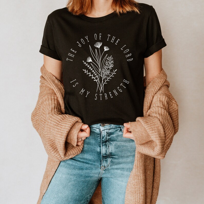 May include: Black t-shirt with a white floral design and the text "The Joy of the Lord is My Strength".