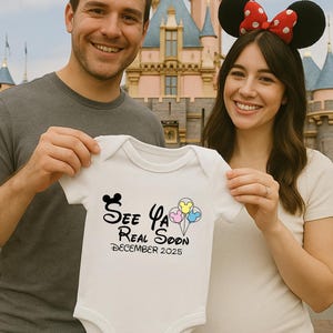May include: A couple in front of Sleeping Beauty's castle at Disneyland, holding a white onesie with the text "See Ya Real Soon December 2025" and a Mickey Mouse ear design. The onesie has a pink, blue, and yellow balloon design.