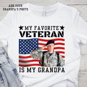 May include: White t-shirt with the text "My Favourite Veteran is My Grandpa" and an American flag with a soldier saluting in front of it.  There is a space to add a photo.