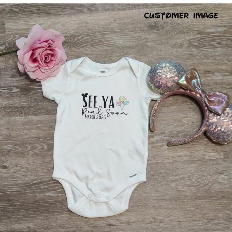 May include: White baby onesie with black text that reads "See Ya Real Soon March 2025" and a cartoon Mickey Mouse head. There are also colorful cartoon balloons above the text.