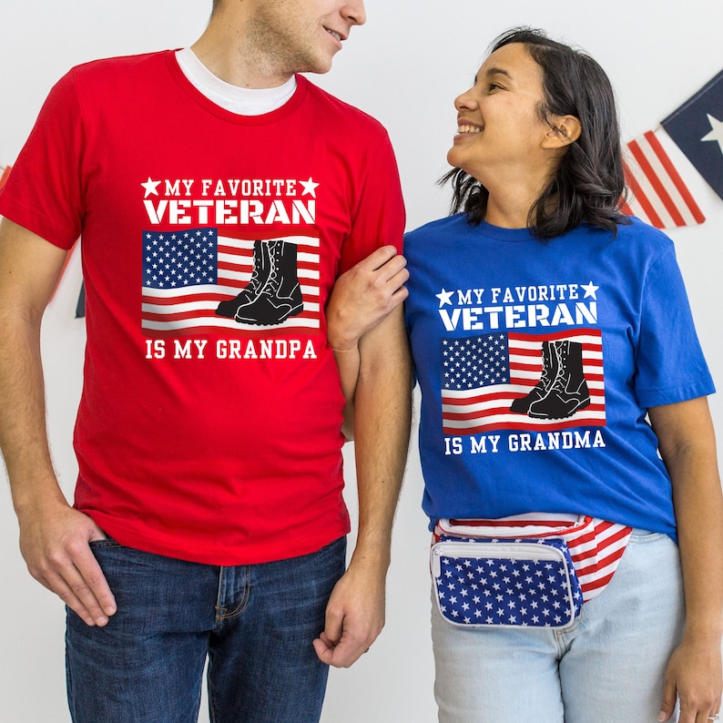 May include: Two people wearing red and blue t-shirts with the text "My Favourite Veteran is My Grandpa" and "My Favourite Veteran is My Grandma". The shirts feature an American flag and a pair of military boots.