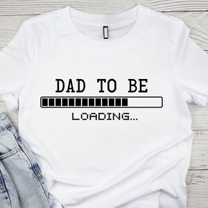 May include: White t-shirt with black text that reads "DAD TO BE" with a progress bar underneath that says "LOADING..."