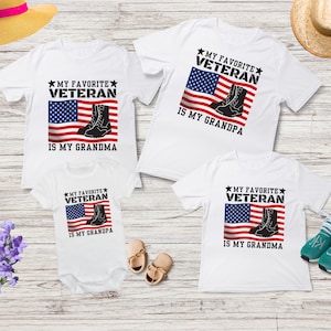 May include: Three white t-shirts featuring an American flag and boots design. The text on the shirts reads "My Favourite Veteran is My Grandma" and "My Favourite Veteran is My Grandpa".