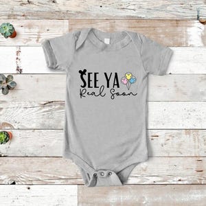 May include: A gray baby onesie with black text that reads "See Ya Real Soon" and a black Mickey Mouse head with three colorful Mickey Mouse head balloons.