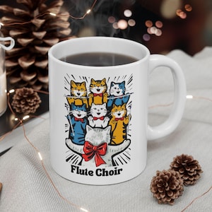 May include: White ceramic mug featuring a colourful illustration of cats playing musical instruments. The text "Flute Choir" is printed on the mug.