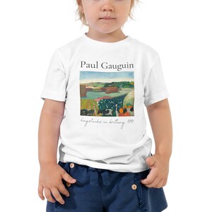 Peut inclure: T-shirt blanc pour enfant en bas âge avec une peinture de Paul Gauguin intitulée "Haystacks in Brittany, 1890". La peinture représente un paysage avec des meules de foin, des vaches et un ciel bleu.