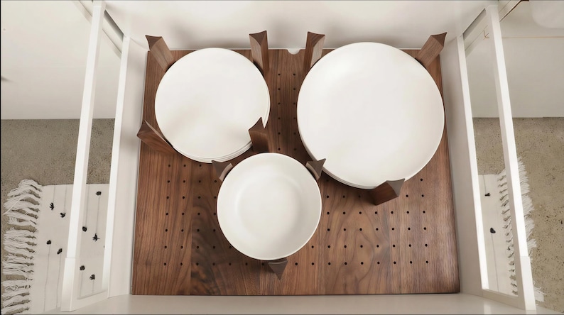 Może przedstawiać: Drewniany organizer do szuflady z trzema białymi ceramicznymi talerzami. Organizer wykonany jest z ciemnego drewna i ma wycięcia, kt&oacute;re utrzymują talerze na miejscu. Talerze są w r&oacute;żnych rozmiarach.