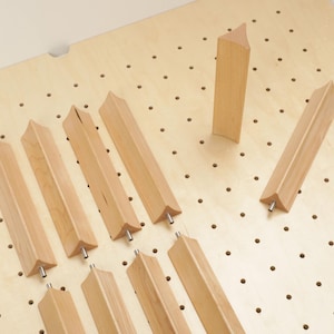 May include: A collection of unfinished wooden furniture legs with a unique, angled design. The legs are light brown and feature a metal screw at the base for attachment. They are arranged on a light-colored wooden surface with evenly spaced holes.