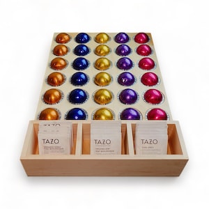 May include: A wooden storage organiser with a grid of 36 compartments for holding coffee pods. The organiser has a drawer with three compartments for storing tea bags. The tea bags are labelled "TAZO Organic Chai/Chai Biologique", "TAZO Organic Zen/Zen Biologique", and "TAZO Earl Grey".