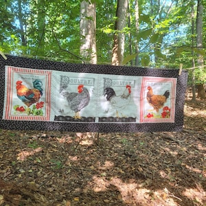 May include: A black and white fabric panel with a red and white striped border. The panel features three different images of roosters, each with the word "Poultry" printed above it.