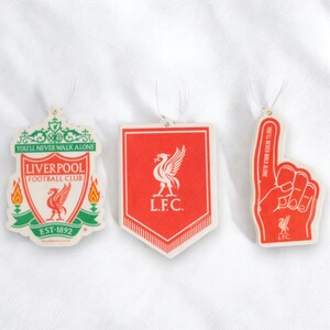 May include: Three red and white Liverpool Football Club car air fresheners. The first is a crest with the text "You'll Never Walk Alone", "Liverpool Football Club", and "EST-1892". The second is a shield with the text "L.F.C.". The third is a raised finger with the text "You'll Never Walk Alone" and "LFC".
