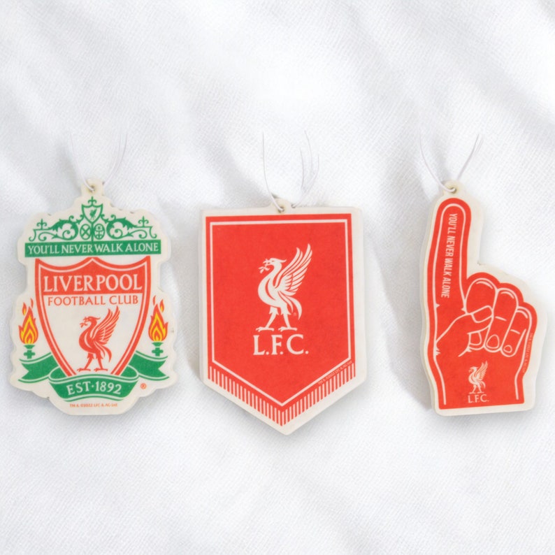 May include: Three red and white Liverpool Football Club car air fresheners. The first is a crest with the text "You'll Never Walk Alone", "Liverpool Football Club", and "EST-1892". The second is a shield with the text "L.F.C.". The third is a raised finger with the text "You'll Never Walk Alone" and "LFC".