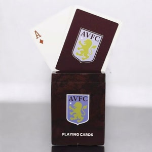 May include: A deck of playing cards with the Aston Villa Football Club logo. The box and card backs are a dark burgundy color, with the club's crest in yellow and blue. The Ace of Diamonds is visible.