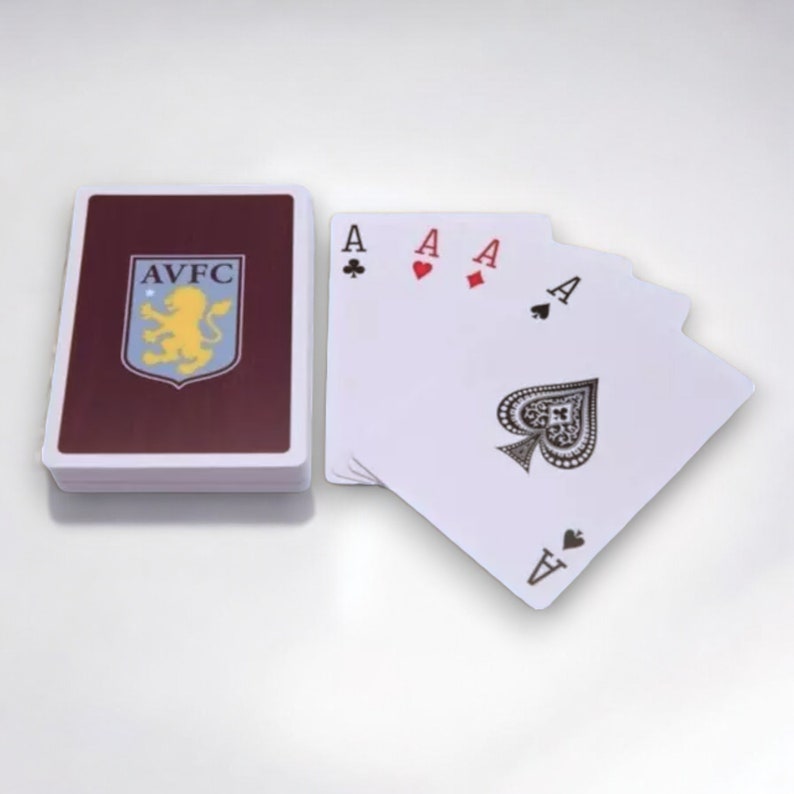 May include: A pack of playing cards featuring the Aston Villa Football Club logo on the maroon back. Four aces are displayed, showing the suits of clubs, hearts, diamonds, and spades. The cards are white.