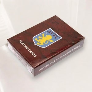 May include: A sealed deck of playing cards with a maroon and brown textured design. The top of the box features the Aston Villa Football Club logo in blue, yellow, and white. The words "PLAYING CARDS" are printed in white.