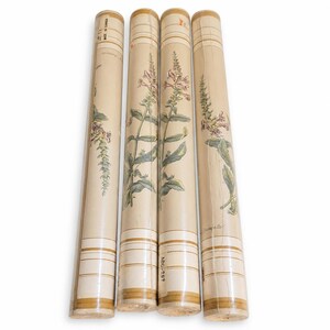 May include: Four rolls of wallpaper featuring a cream background with a botanical print of tall, slender flowering plants in shades of green, pink, and brown. Each roll has horizontal brown stripes at the top and bottom and text including MADE IN CANADA.