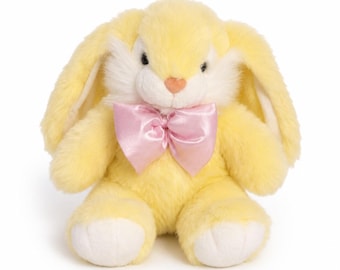 May include: A plush stuffed animal in the shape of a rabbit with soft yellow fur, long floppy ears, and white accents on the face and feet. The rabbit features a small pink nose, dark eyes, and a shiny light pink satin bow tied around its neck.