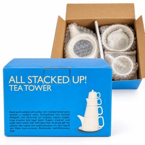 Puede incluir: Una caja de cartón azul con la etiqueta ALL STACKED UP! TEA TOWER y un gráfico de un juego de té de cerámica apilable. Dentro de la caja abierta, una tetera, lechera, azucarero y taza de cerámica blanca están envueltos en plástico.