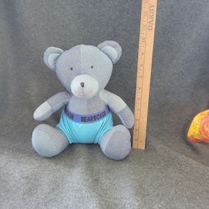 Könnte beinhalten: Ein Stoffbär aus blauem und grauem Patchwork-Stoff. Der Bär trägt blaue Shorts mit dem Aufdruck "BEARBOXER". Ein Holzlineal liegt neben dem Bären.