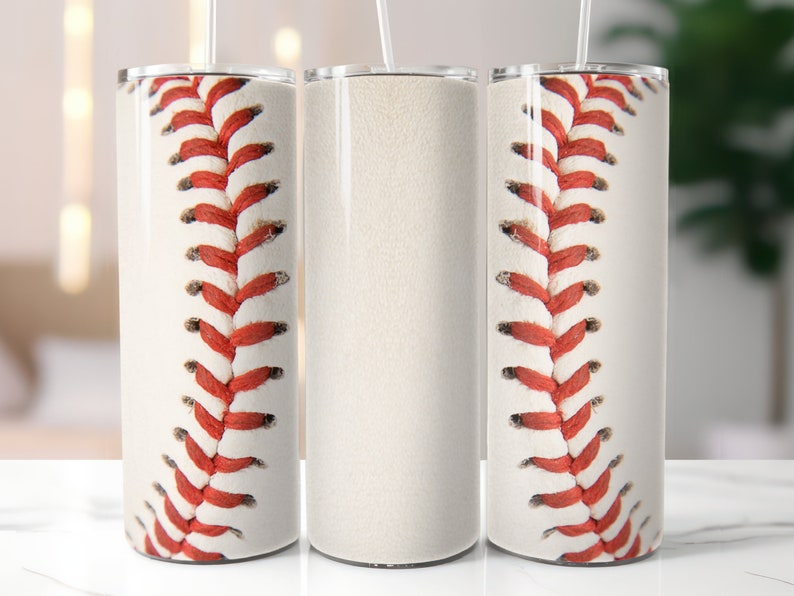 Puede incluir: Un vaso cil&iacute;ndrico con una superficie blanca y un patr&oacute;n repetitivo de costuras de b&eacute;isbol rojas que envuelve el exterior. El vaso incluye una tapa transparente y una pajita fina y recta que sobresale del centro de la parte superior.