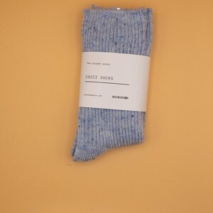 Puede incluir: Un par de calcetines moteados azules y blancos con una etiqueta blanca que dice "The coziest socks."  "COZZI SOCKS" y "cozziapparel.com" est&aacute;n impresos en la etiqueta.
