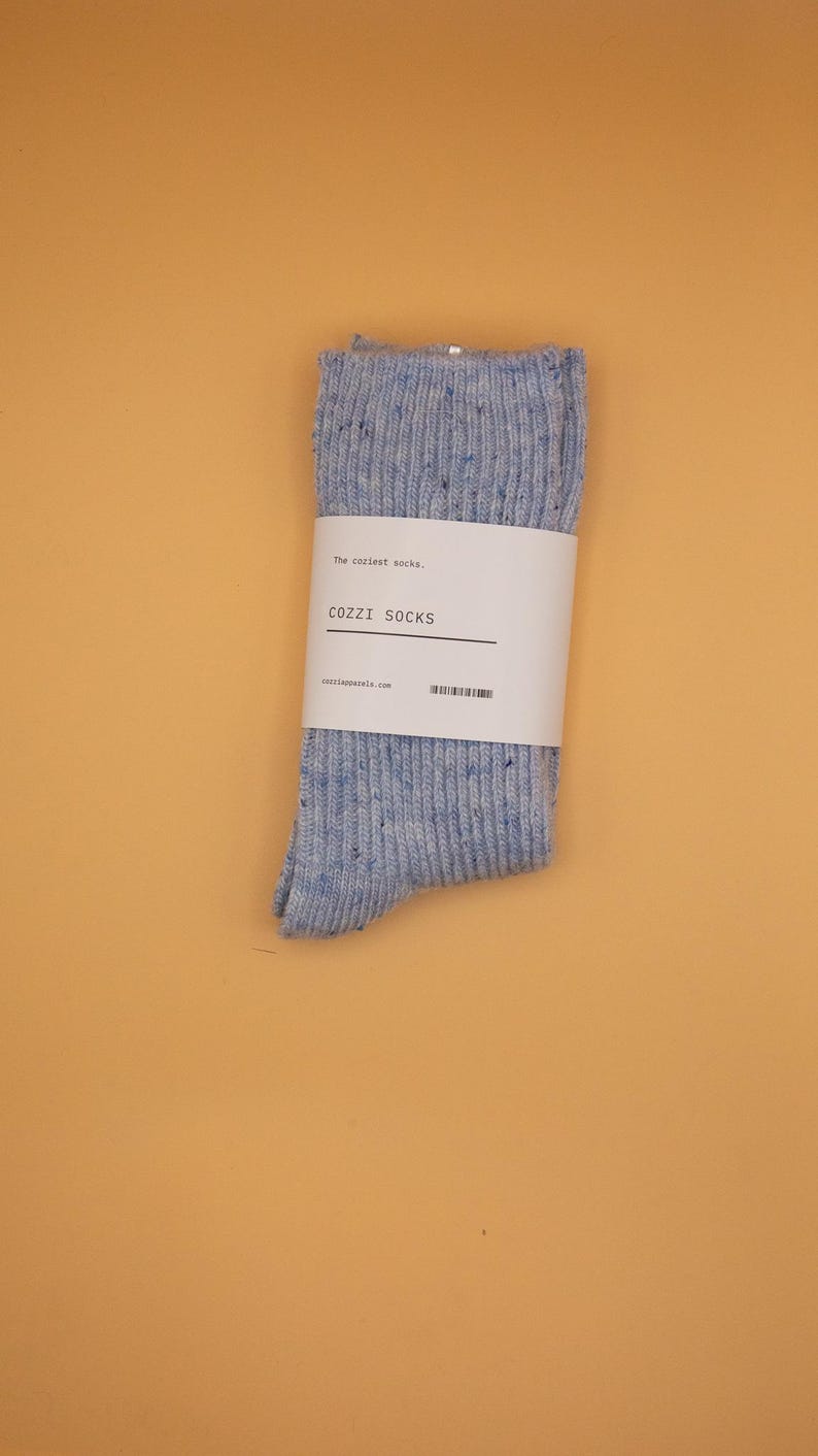 Puede incluir: Un par de calcetines moteados azules y blancos con una etiqueta blanca que dice "The coziest socks."  "COZZI SOCKS" y "cozziapparel.com" est&aacute;n impresos en la etiqueta.